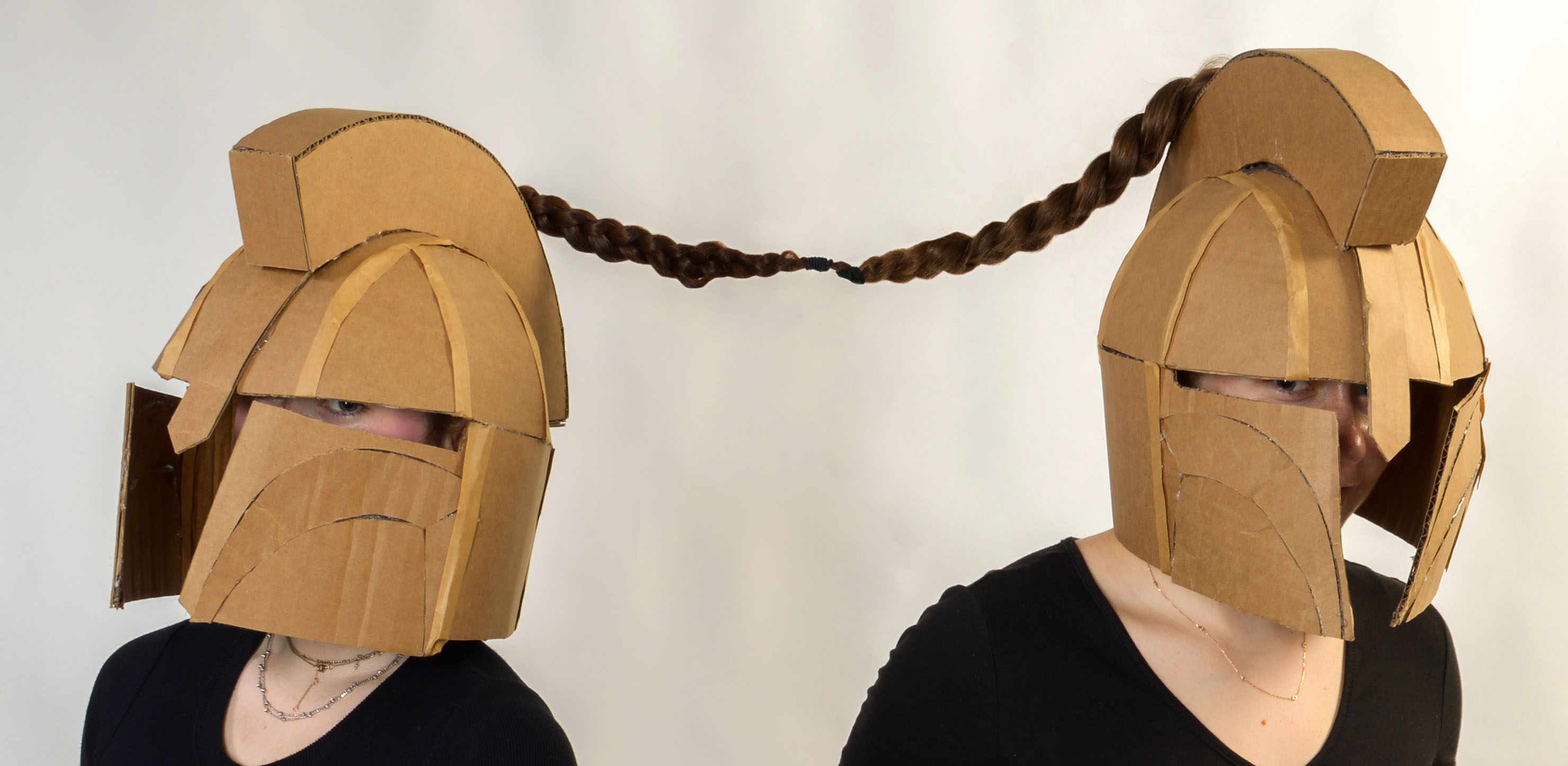 two figures wearing cardboard helmets with their pony tails tied together