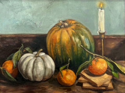 two pumpkins and three oranges on a table with a lit candle in the background